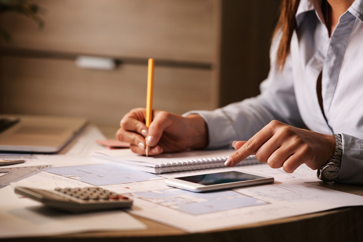 Unrecognizable businesswoman using smart phone while writing notes in the office.