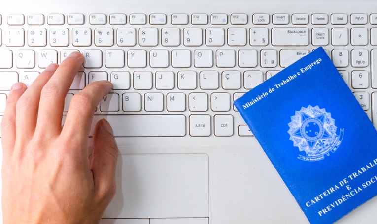 Person looking for job on the internet with a Brazilian work card next to him on the notebook. Working in the home office.